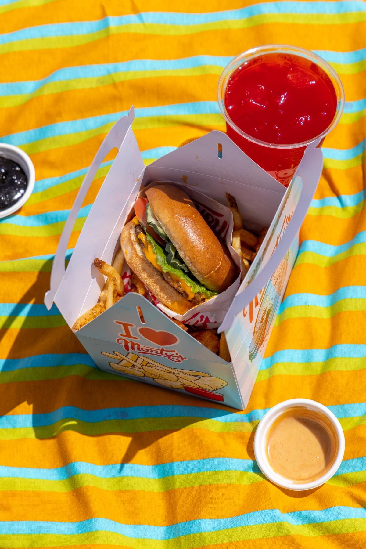 A burger and fries in a container next to a cup of red liquid.