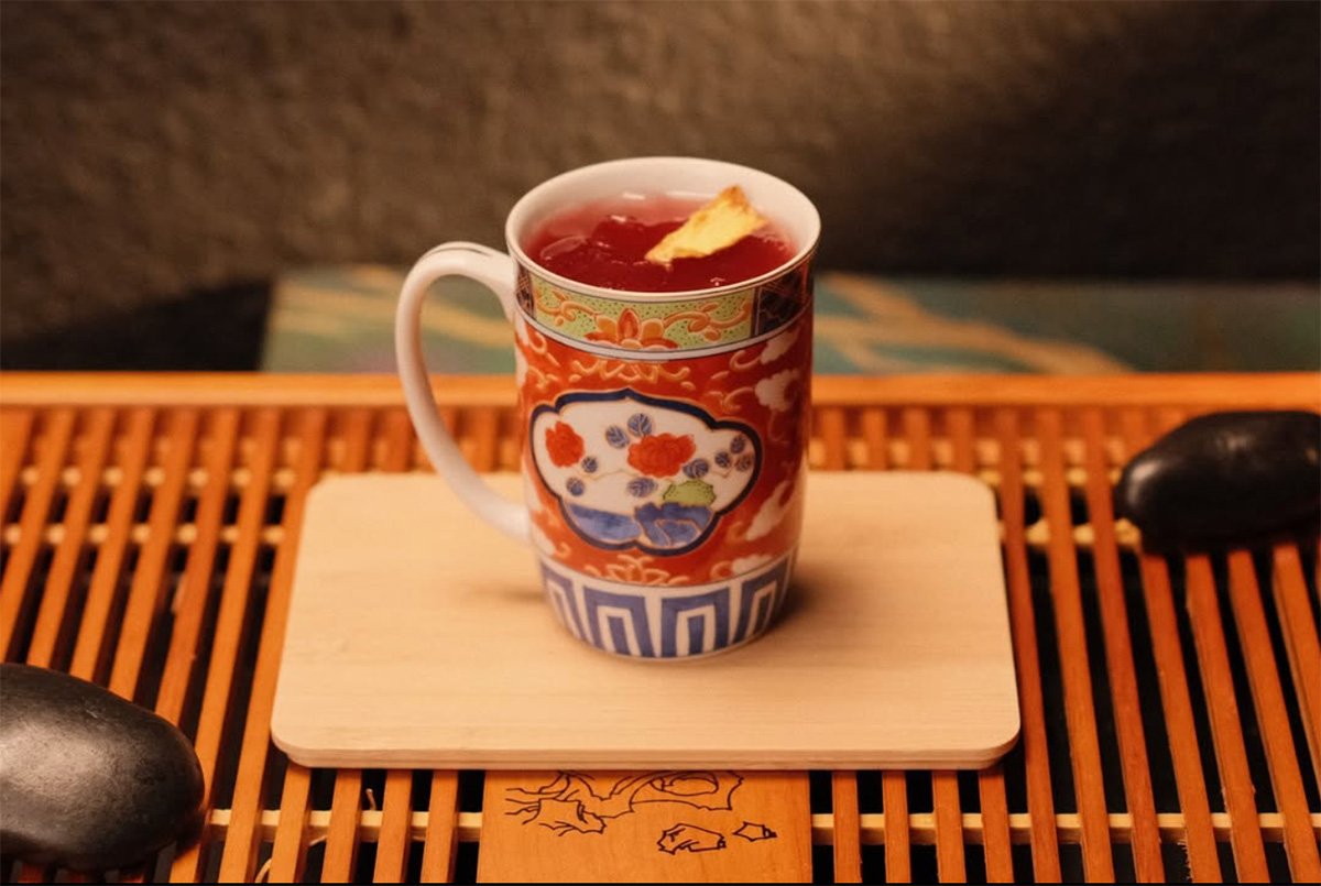 Tea in an ornate red and blue cup sits on a wooden mat.