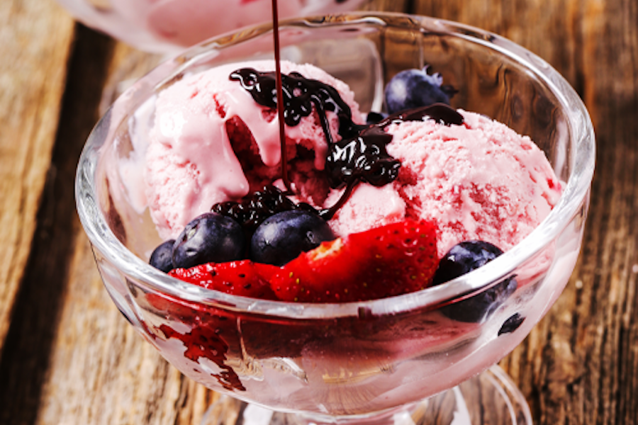 A close up shot of strawberry ice cream with berries and chocolate syrup