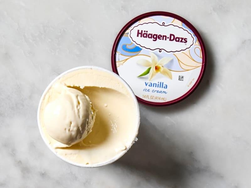 overhead shot of a pint of Haagn-Dazs vanilla ice cream, with the lid off and sitting to the right of the pint.